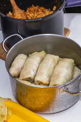 Women cook cabbage rolls while standing at the table and put them in a pot.