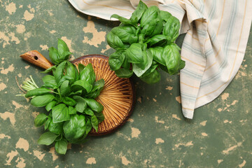 Wooden board with fresh green basil leaves on color background
