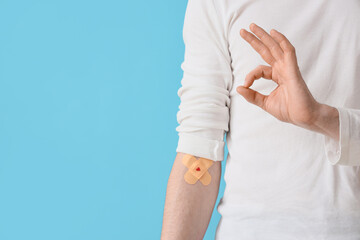 Male blood donor with applied patches showing OK on blue background, closeup