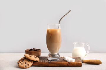 Glass of iced latte with sweet cookies and jug of milk on white background