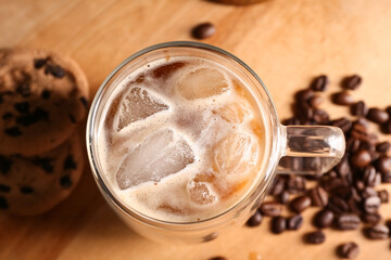 Glass cup of iced latte with sweet cookies and coffee beans on wooden background, closeup