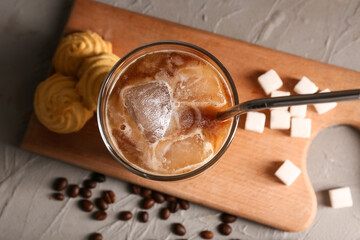 Glass of iced latte with sweet cookies and cubes of sugar on grey background