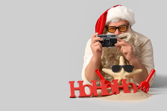 Santa Claus with photo camera and beach accessories on light background. Christmas in July