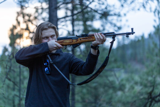 Young man aiming a rifle in the forest setting.