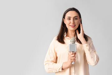 Female reporter in earphone with microphone on light background