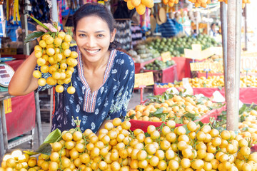 A young woman holds a tropical fruit - the Burmese grape at the market, Thailand