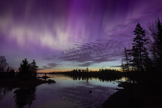Northern lights glow over a lake in Minnesota in as the dawn on the horizon compliments the shining rainbow of Aurora light