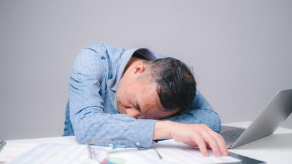 The tired businessman, a sleepy man with a headache, slumps over his desk in the office, struggling...