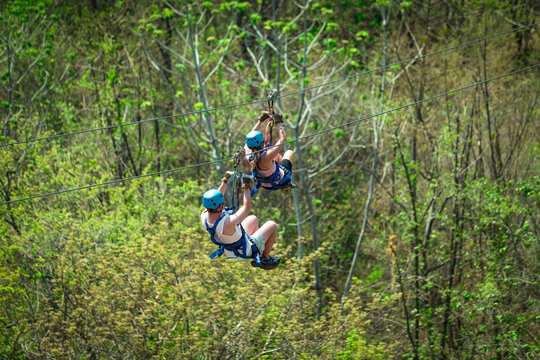 A couple riding a zipline in Costa Rica while on vacation. View from behind as the tourists zip down a jungle mountain on an adventure tour.