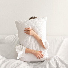 Person embracing white pillow, hiding face behind, sleep, rest and relax, comfortable bedding...