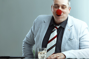 Clown-nosed man at desk, whiskey visible