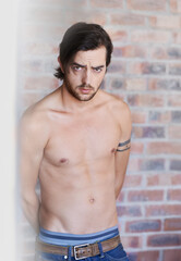 Shirtless, portrait and man in home with tattoo, skincare or confidence on brick wall in apartment. Male, model and body art with topless person in house with pride and relax in calm morning