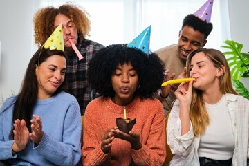 Multiracial happy friends celebrating a birthday party with party horns and hats.