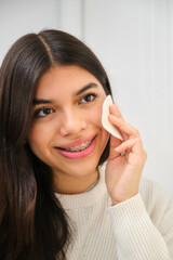 Female Latin teenager with braces using make up cotton pad.