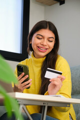 Latin female teenager with braces buying online in a smartphone with a credit card.