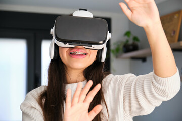 Female Latin teenager with braces using VR headset at home.