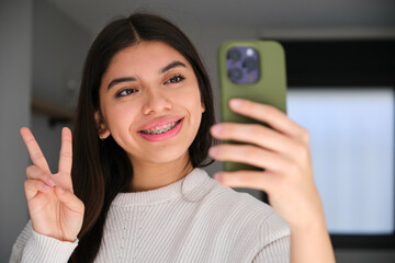 Female Latin teenager with braces taking a selfie with her smartphone.