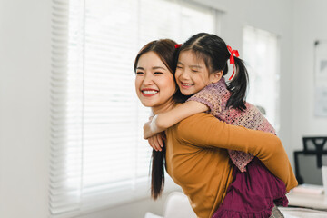 Little girl enjoying a piggyback ride with young mother at living room. Family enjoy playtime...