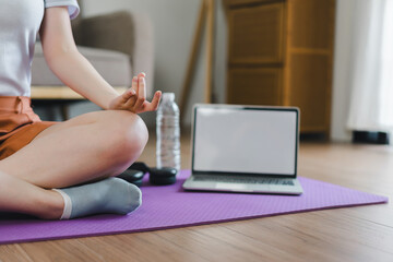 Young Asian woman at home doing yoga in front of open laptop, repeating instructions by...