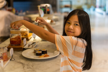 breakfast buffet by asian child hungry or kid girl scooping picking up sushi and pickles kimchi on...