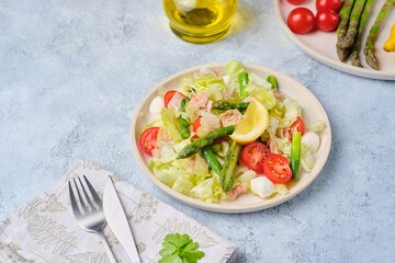 Salad with asparagus, canned tuna, tomatoes and mozzarella cheese on a ceramic plate on a light concrete background. Healthy eating, lifestyle.
