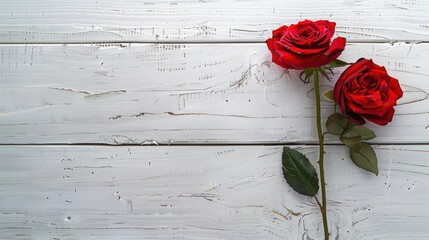 Two vibrant red roses with green leaves lying across a textured white wooden surface, suggesting romance or a special occasion