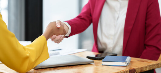 Two businesswomen hold hands on a table while finishing a work briefing. An agreement or partnership to invest in a financial business online marketing startup business idea.