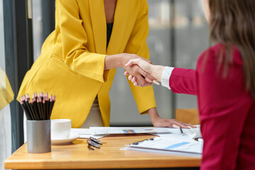 Two businesswomen hold hands on a table while finishing a work briefing. An agreement or...