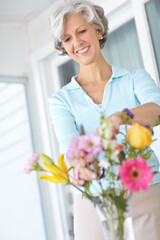 Happy, senior and woman arrange flowers in home, vase and creativity in spring of retirement. Floral, bouquet and elderly person with gardening hobby or relax with daisy wildflowers in house