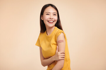 young asian women smiling after getting a vaccine, holding down her shirt sleeve and showing her...