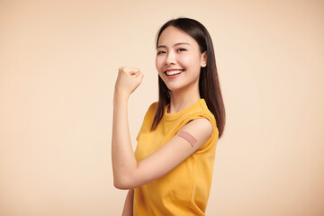 young asian women smiling after getting a vaccine, holding down her shirt sleeve and showing her...
