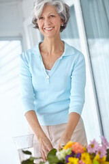 Senior woman, vase and flowers in home with thinking, decision and natural decoration in morning. Mature person, happy and style with floral bouquet, memory or glass container in house for retirement