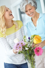 Laughing, mom and happy woman with flowers in house together with love, joke or pride for gardening. Mothers day, senior or funny daughter bonding in home with family, parent or gift present in USA