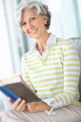 Senior woman, book and portrait in home on sofa with smile, literature or relax with poetry in...