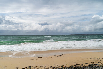 Plage de sable et galets, eaux océaniques émeraude et écume blanche sur le sable sous un ciel...