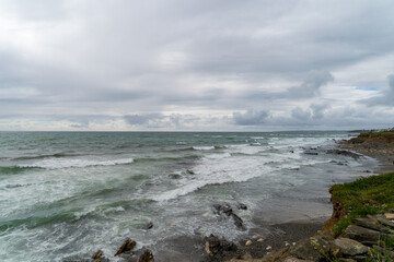 La côte bretonne sous un ciel couvert, avec des vagues couleur émeraude et de l'écume blanche .