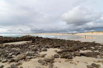 La plage de La Torche, un lieu de surf célèbre, avec de gros galets au premier plan sous un ciel...