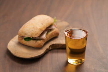 Ciabatta sandwich with ham and pesto and glass of cider on wood table