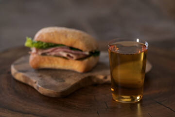 Ciabatta sandwich with ham and pesto and glass of cider on wood table