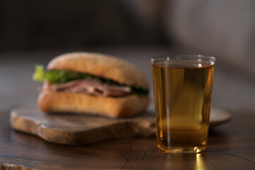 Ciabatta sandwich with ham and pesto and glass of cider on wood table