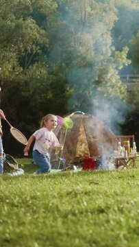 Vertical shot of a multi-generational family camping in nature, playing bagminton, lighting a fire for barbecue and spending time together