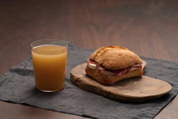 Sandwich with bresaola, mozzarella and pest on olive board with orange juice