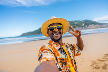 African american man taking selfie gesturing victory on beach