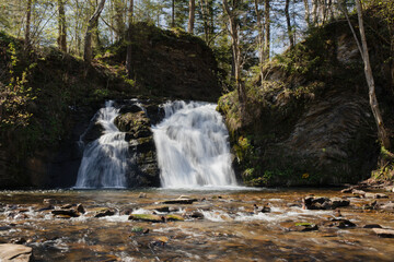 a waterfall falls from stones into a forest lake, clear water, on the slopes of trees, greenery, moss, sun glare, shadows, splashes, walk, thicket, travel, beauty