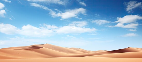 Scenic desert sand dunes with a clear blue sky and clouds perfect for a copy space image