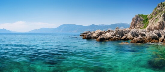 Fototapeta premium Scenic view with rocks in clear turquoise ocean green mountains in backdrop ideal for copy space image