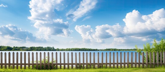 Obraz premium A wooden fence stands by the river against a backdrop of a sunny blue sky with fluffy clouds providing a charming scene with copy space image