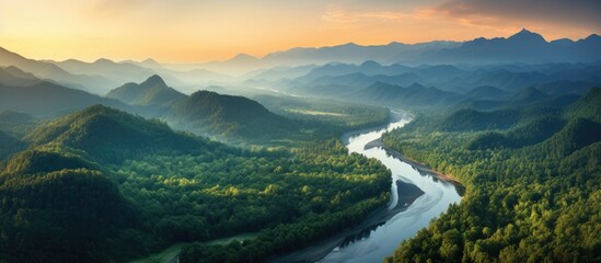 Aerial view of a mountain range and tall forest by a river during a summer evening with orange...