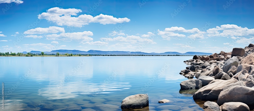 Poster scenic lake view with rocks in the foreground and a vast expanse of water reflecting the sky ideal f