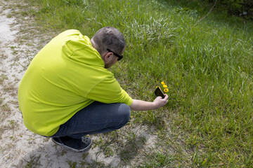  A man in a vibrant yellow shirt and cap is crouched down in a field of green grass and yellow...